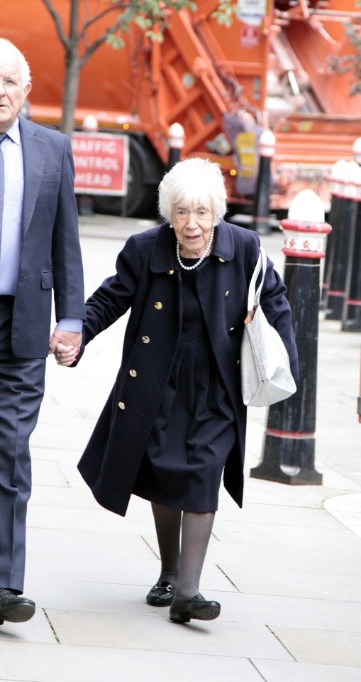 an elderly woman is walking down a sidewalk holding hands with a man in a suit