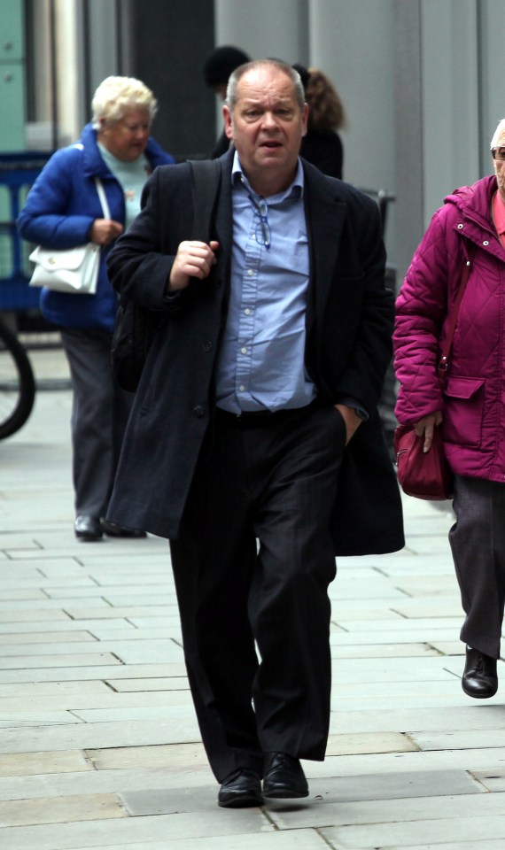 a man in a suit walks down a sidewalk with his hands in his pockets