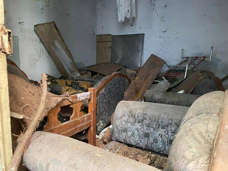 a messy room with a couch and a bed with the word jesus written on the wall