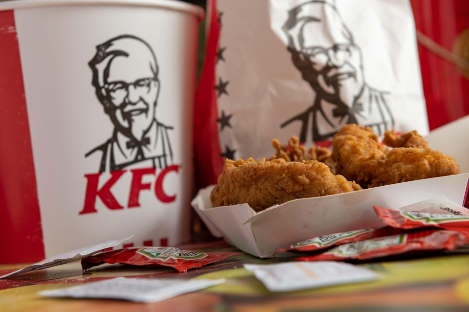 2BXNC4R Kentucky Fried Chicken, KFC, fillets with packets of tomato ketchup on a table top and bucket and bag with the company logo and trademark.