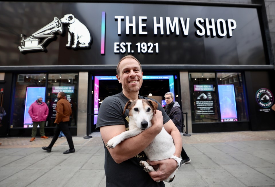 a man holding a dog in front of the hmv shop