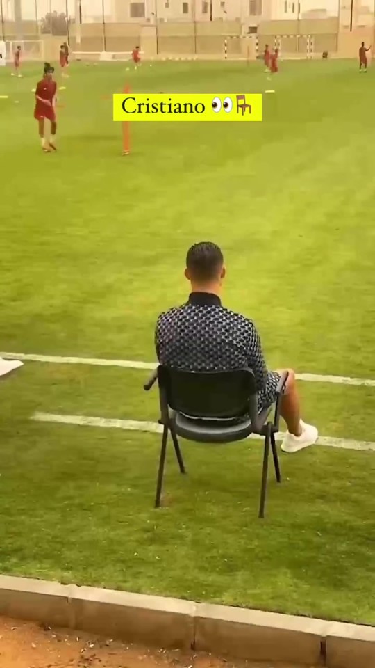 a man is sitting in a chair on a soccer field with a sign that says cristiano on it