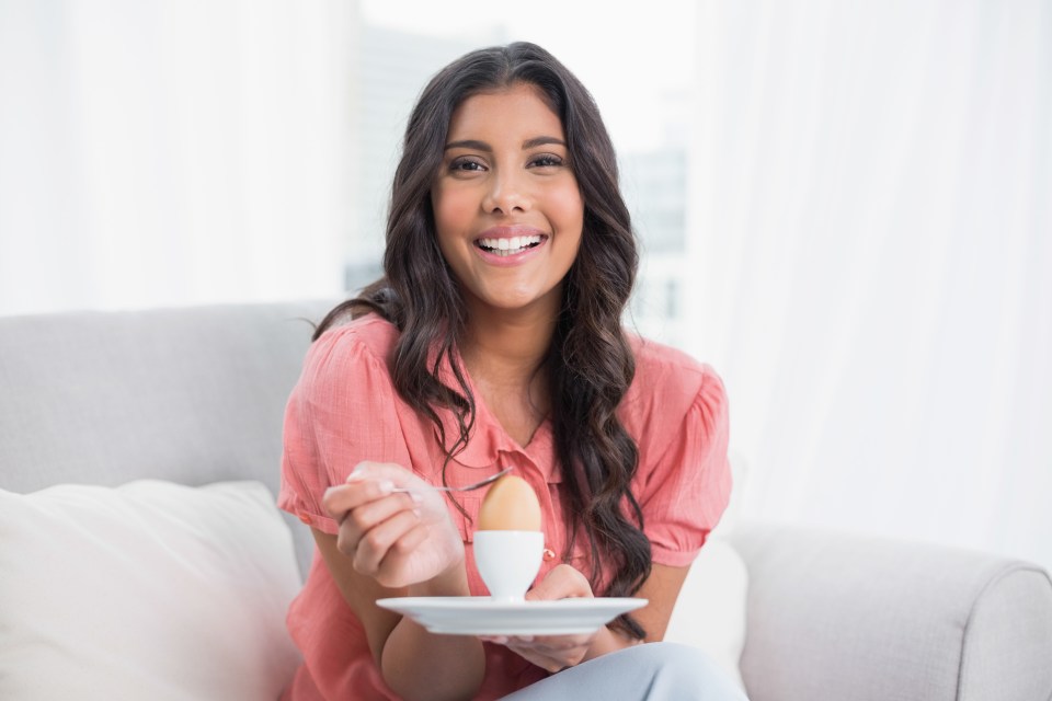 a woman is sitting on a couch eating an egg with a spoon