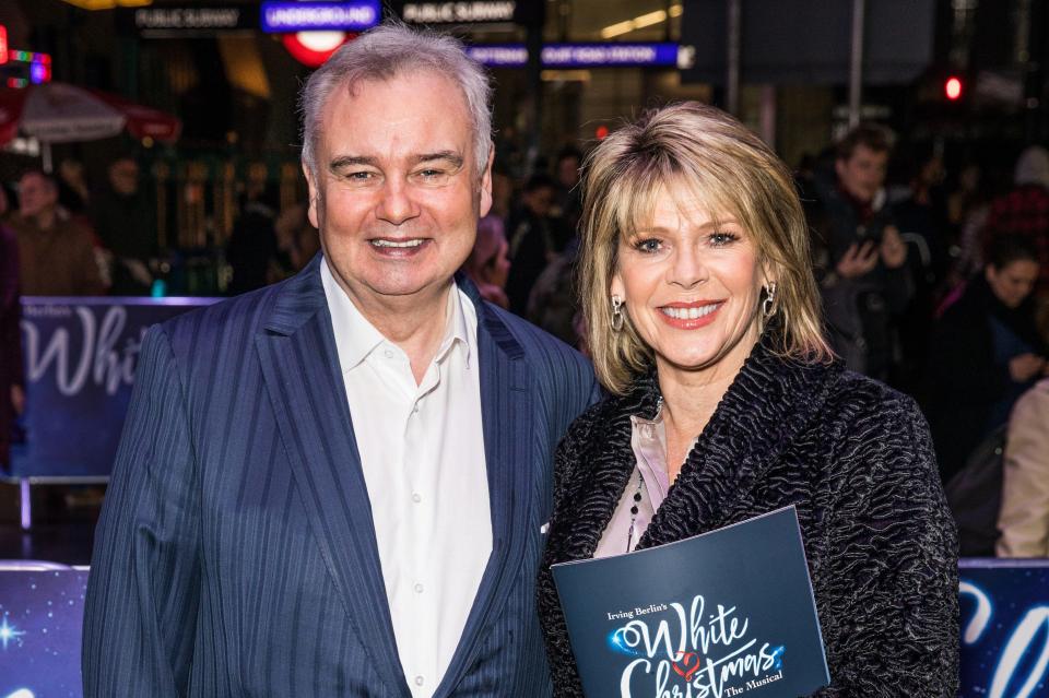 a man and a woman are standing next to a white christmas sign