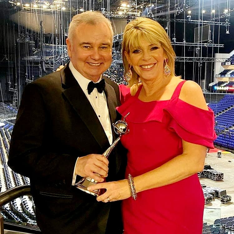 a man in a tuxedo holds a trophy next to a woman in a red dress