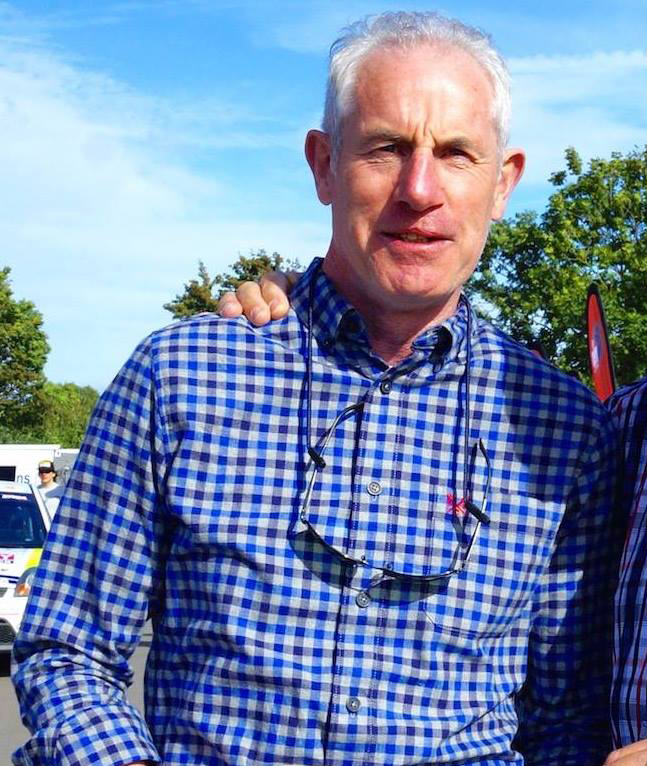 a man wearing a blue plaid shirt has a pair of glasses around his neck