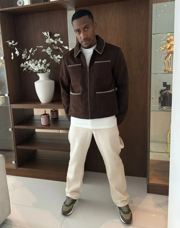 a man in a brown jacket stands in a living room