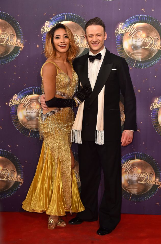 a man in a tuxedo and a woman in a gold dress pose on a red carpet