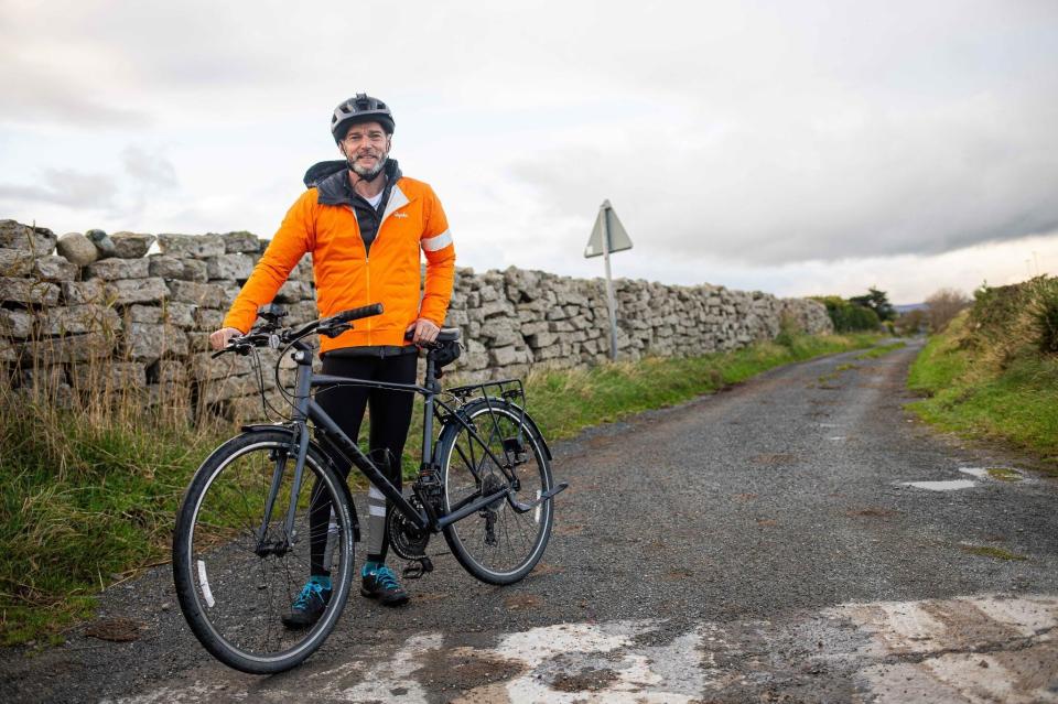 a man in an orange jacket stands next to a bicycle