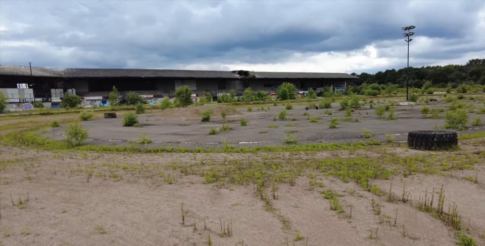 a tire in the middle of a dirt field with a building in the background