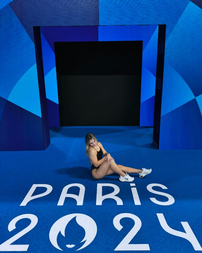 a woman sits on the floor in front of a sign that says paris 2024