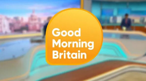 the logo for good morning britain is shown in front of a blurred background of a news studio .