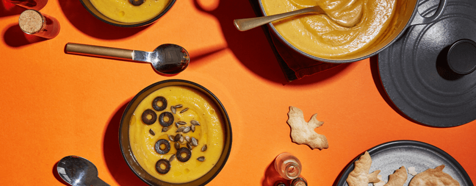 a bowl of soup with olives and pumpkin seeds on top