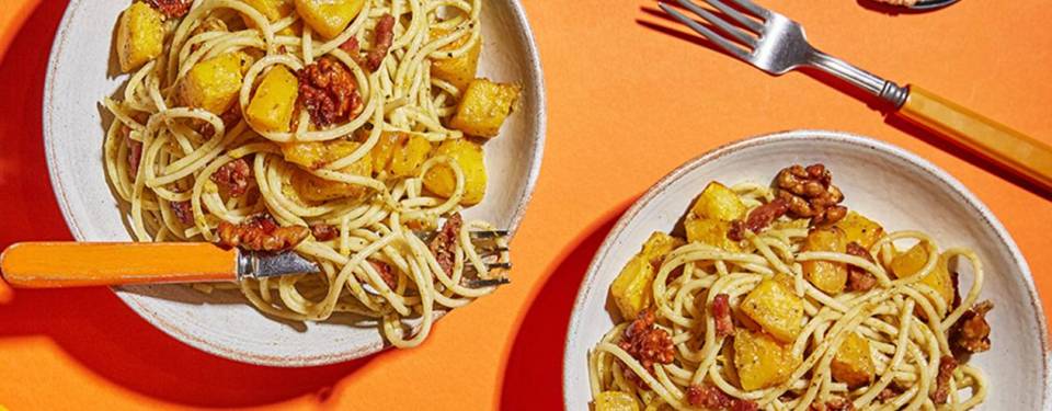 two bowls of pasta with vegetables and a fork on an orange table .