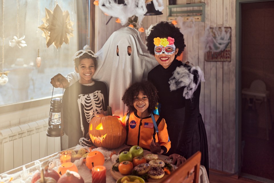 a woman in a mask stands next to two children in halloween costumes