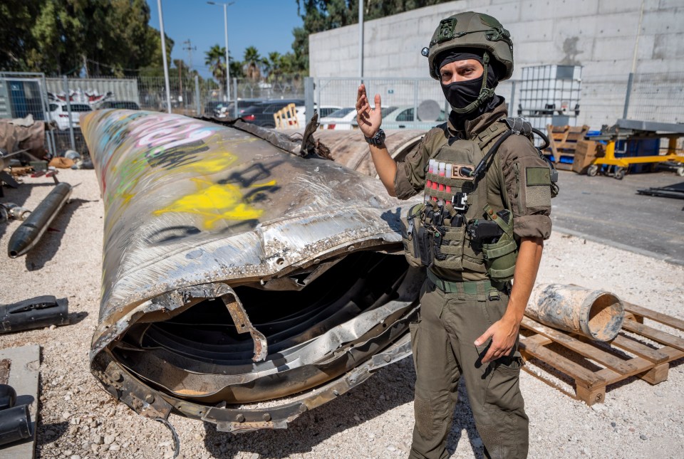 a man wearing a mask and a helmet stands in front of a large pipe with graffiti on it