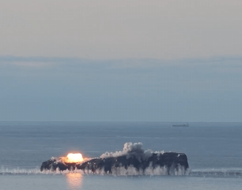 a large rock in the middle of the ocean with smoke coming out of it