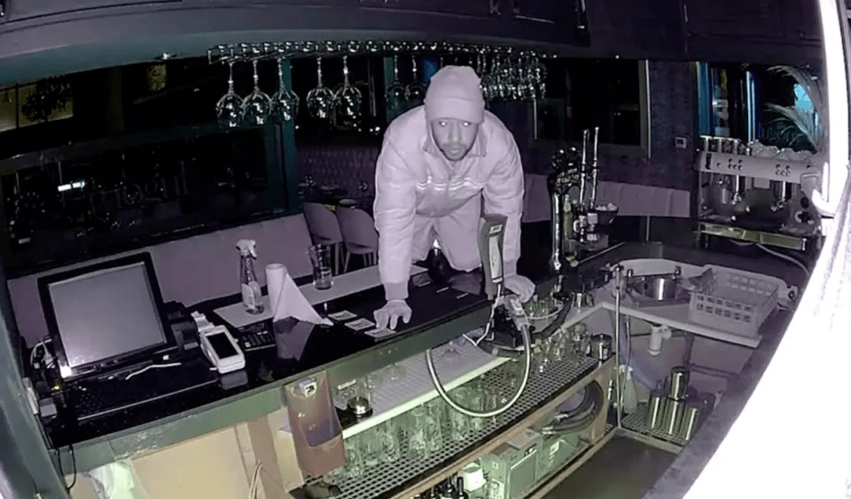 a man in a white hoodie is kneeling at a bar