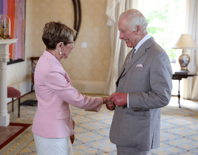 a man in a suit shakes hands with a woman in a pink jacket
