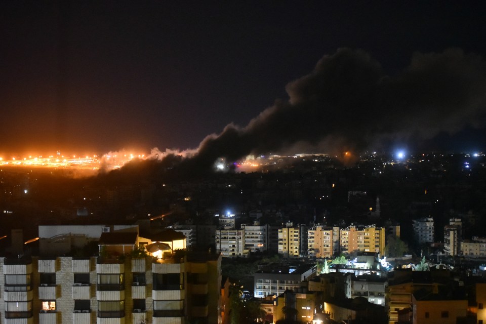 a city at night with smoke coming out of the sky