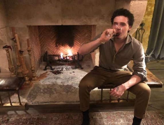 a man is sitting in front of a fireplace drinking a glass of wine