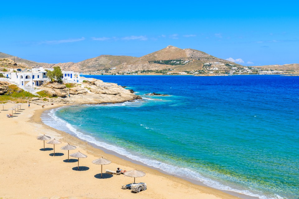 a beach with umbrellas and chairs and mountains in the background
