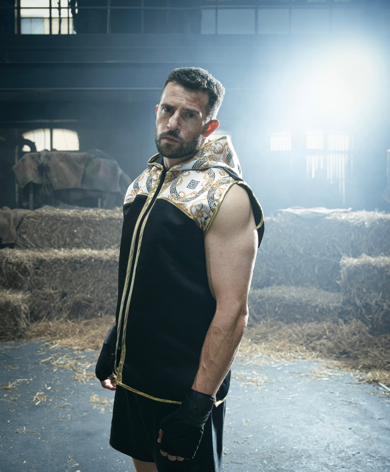 a man in a black and gold boxing outfit stands in front of hay bales