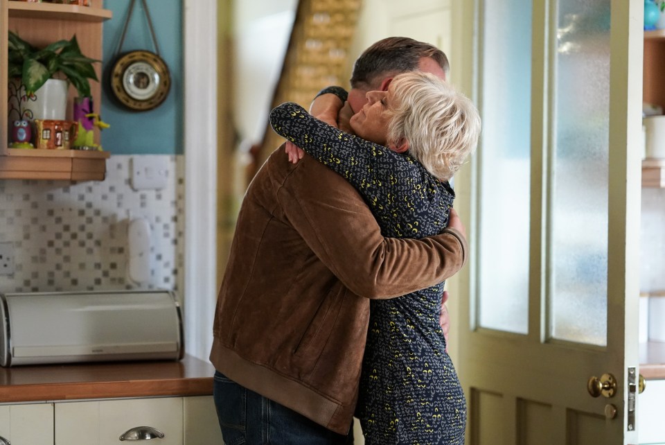 a man in a brown jacket hugging a woman in a kitchen