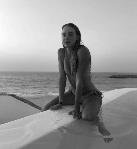 a woman in a bikini is kneeling on a ledge overlooking the ocean .
