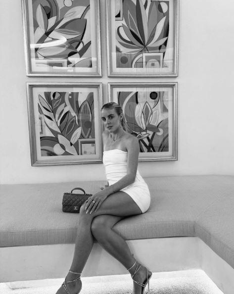 a woman in a white dress is sitting on a bench in front of paintings .