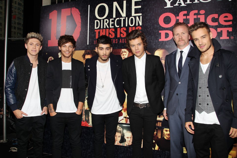 a group of men standing in front of a sign that says one direction