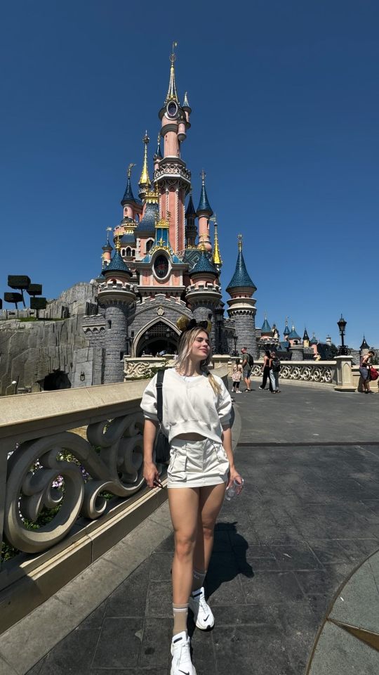 a woman stands in front of the disney castle