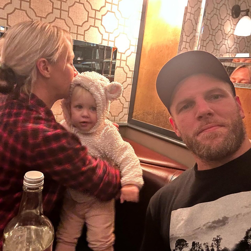 a man and a woman holding a baby wearing a teddy bear outfit