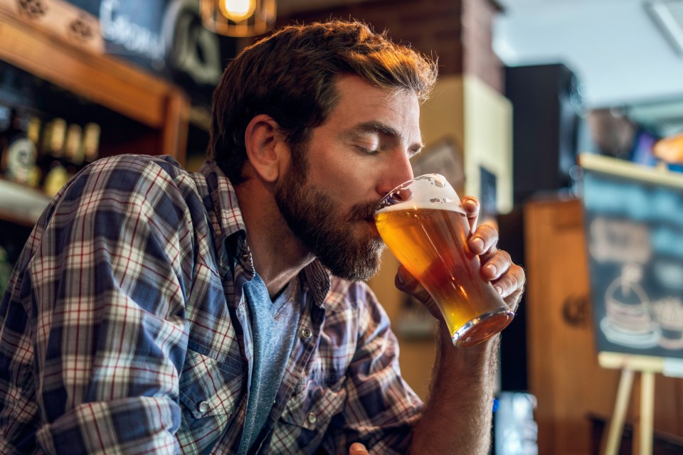 a man in a plaid shirt is drinking a glass of beer