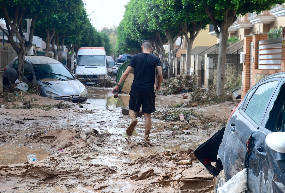 a man walks through a flooded street carrying a bottle of water
