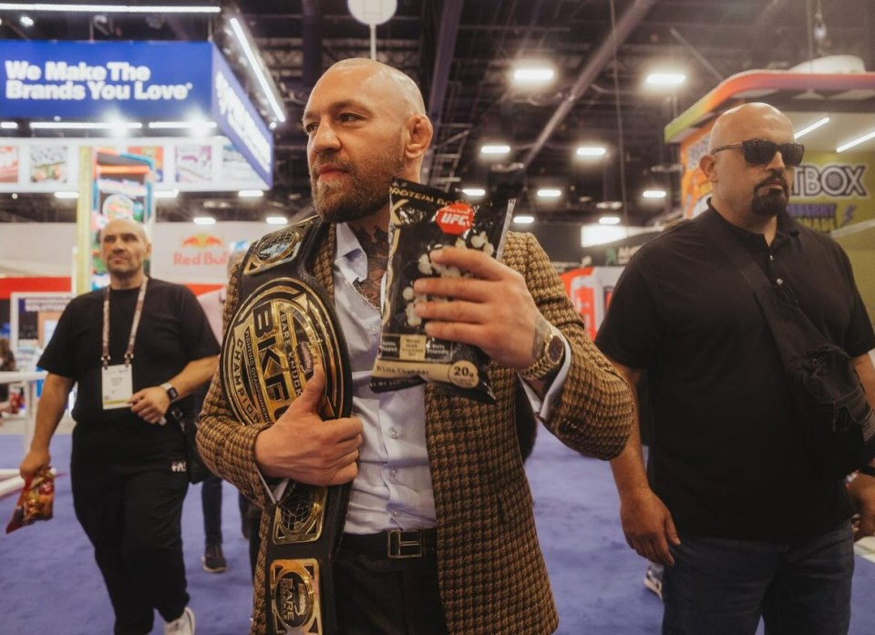 a man wearing a ufc belt holds a bag of popcorn