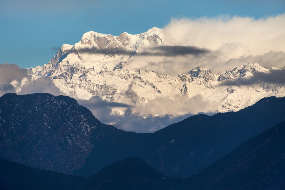 a snowy mountain covered in clouds against a blue sky