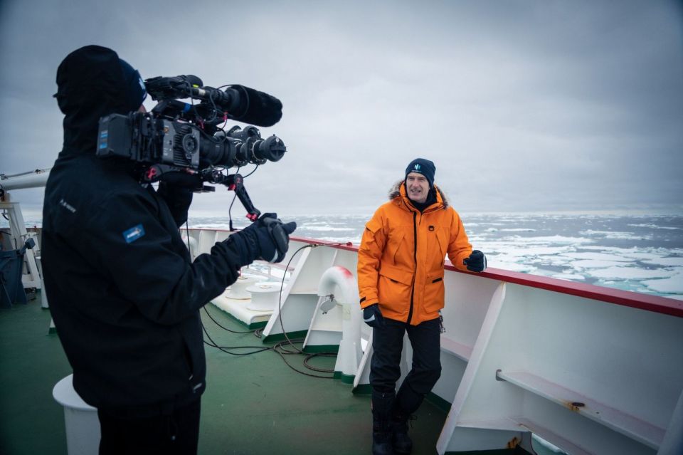 a man in an orange jacket is being interviewed by a cameraman