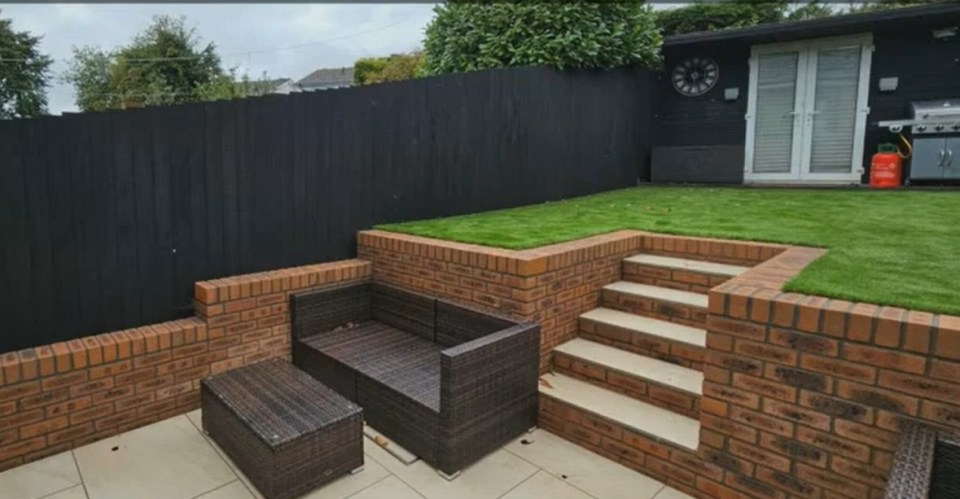 a black fence surrounds a backyard with a clock on the wall