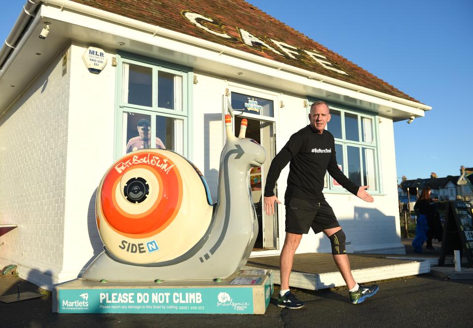 a man stands in front of a snail statue that says please do not climb