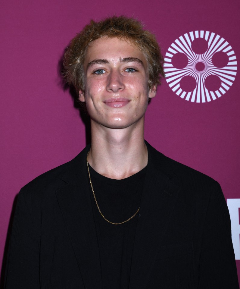 a young man wearing a black jacket and a gold chain