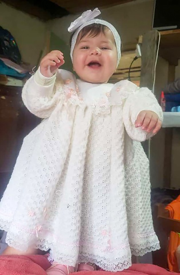 a baby girl wearing a white dress and headband smiles for the camera