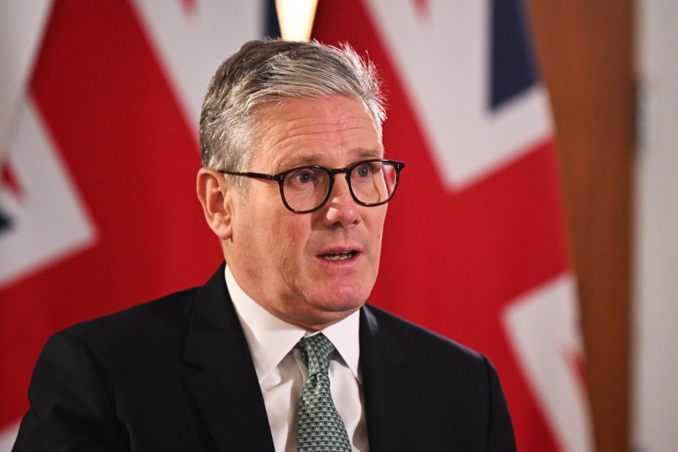 a man wearing glasses and a suit stands in front of a british flag