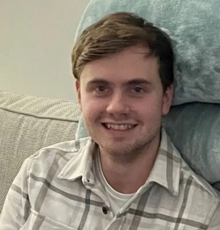 a man in a plaid shirt is smiling while sitting on a couch .