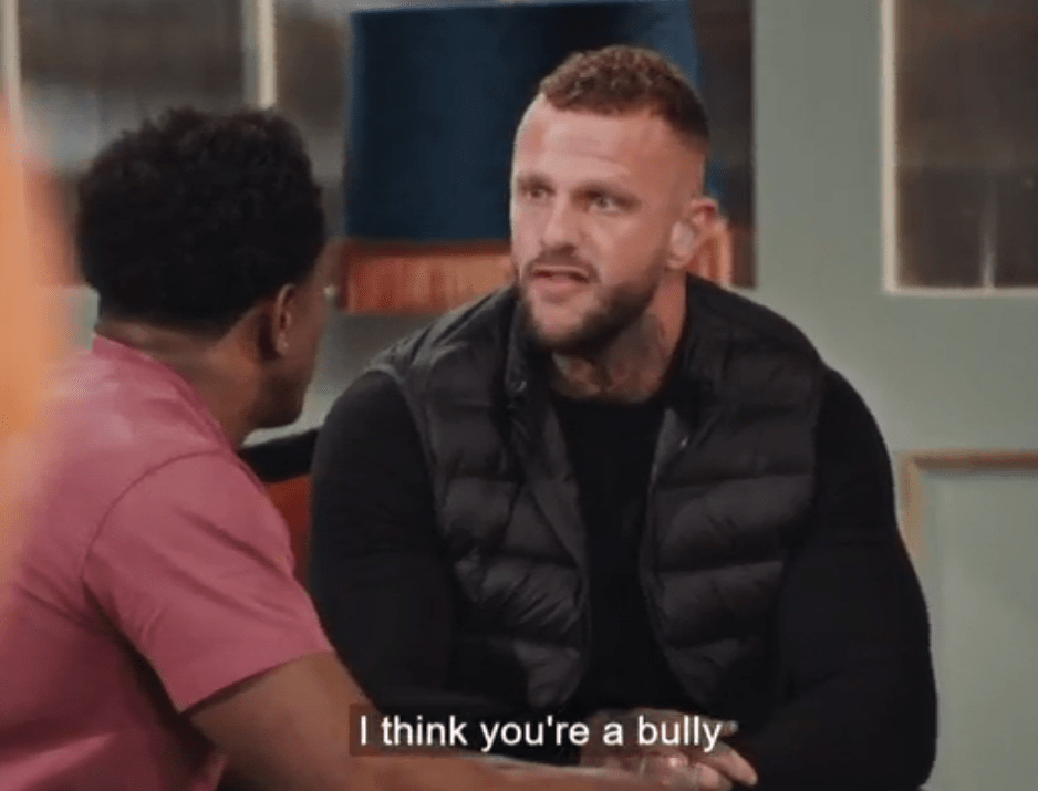 a man in a black vest is talking to another man who is wearing a pink shirt