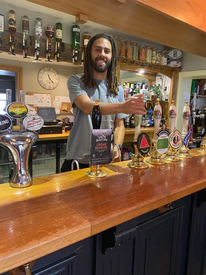 a man stands behind a bar holding a bottle of black lion