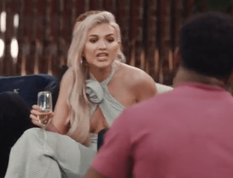 a woman is sitting on a couch holding a glass of wine and talking to a man .