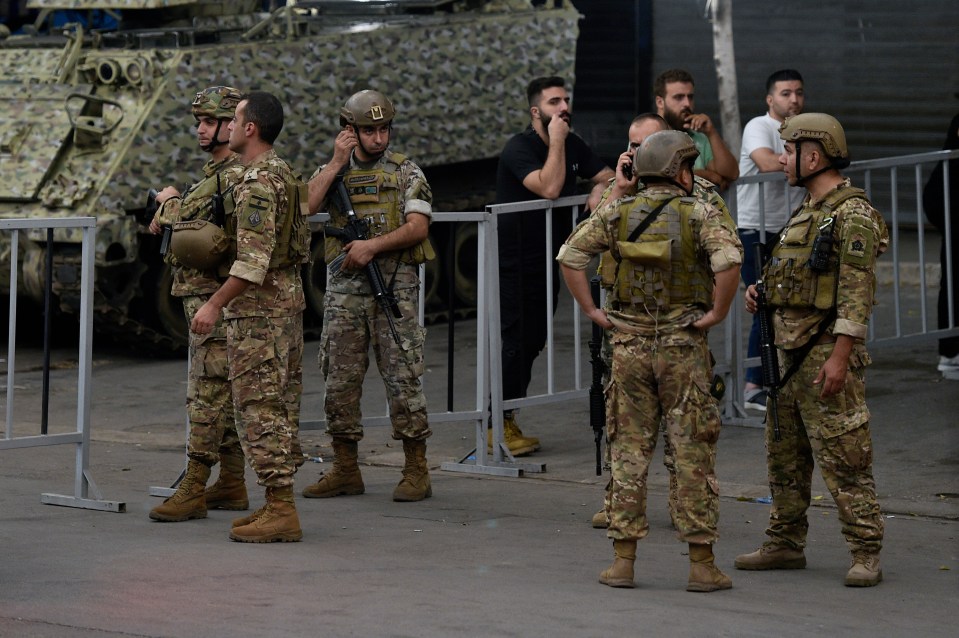 a group of soldiers are standing in front of a fence with a man talking on a cell phone