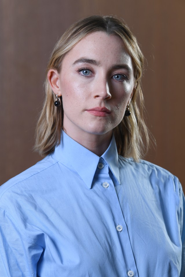 a woman wearing a blue shirt and earrings looks at the camera