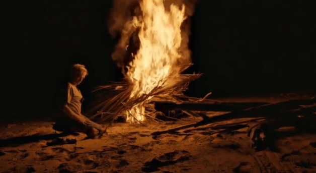 a man is kneeling in front of a large fire